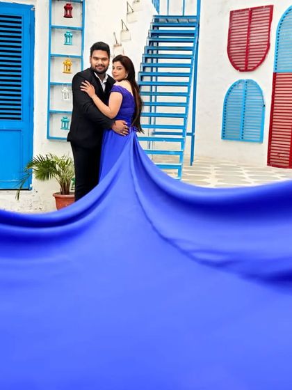 The flowing trail of the royal blue gown fills the foreground, creating a dreamy and immersive effect that draws you into the couple's romantic moment.