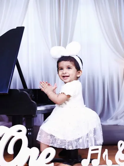 A happy, clapping baby girl at the piano, celebrating her first birthday in style.