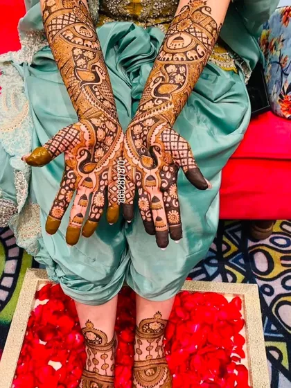 A stunning design with peacocks on the palms and feet, set against a backdrop of red rose petals, highlighting the rich color of the henna.