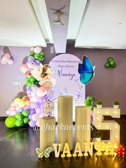 A full view of the enchanting butterfly-themed 5th birthday party. The setup includes a large light-up number '5', custom plinths for the cake, and marquee letters spelling out the birthday girl's name.