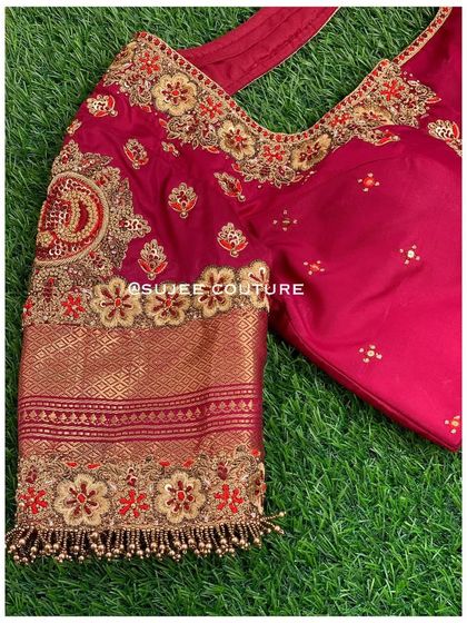 A custom maroon bridal blouse with a sweetheart neckline. The sleeve features a personalized touch with an embroidered initial 'D' inside a traditional motif, surrounded by floral zardozi work.