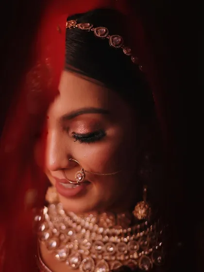A classic bridal portrait, using the red veil to create a soft, intimate frame. This signature shot focuses on the bride's serene expression and detailed makeup.