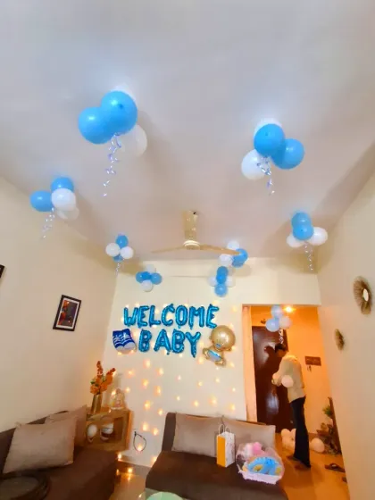 A simple and sweet "Welcome Baby" decoration for a home. The setup includes blue and white helium balloons on the ceiling and blue foil letters on the wall above a display of fairy lights.