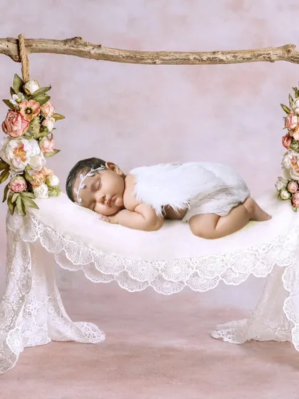 A one-month-old baby girl dressed as an angel, sleeping on a delicate lace hammock.