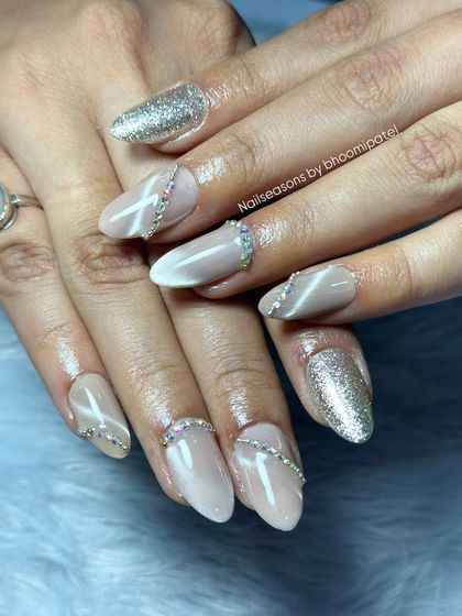 An elegant nude manicure with a cat eye base, silver glitter, and rhinestone accents.