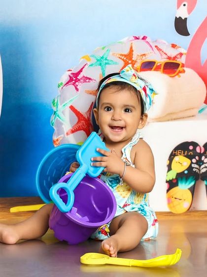 A big, happy smile from our beach baby. She's having a great time playing with all the colorful props in this vibrant setup.