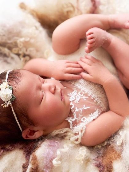 A seven-day-old newborn stretches out on a bed of soft, multi-colored wool, wearing a delicate lace outfit and floral headband.