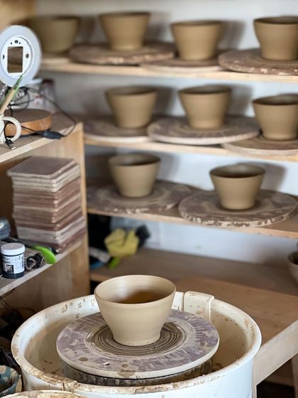 Rows of freshly thrown bowls drying on shelves, a testament to a productive day of production work in the studio.