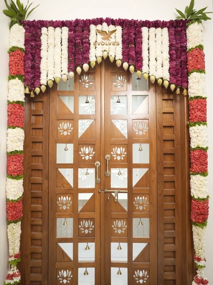 A close-up of a main door decorated with traditional flower garlands, featuring a mix of red, white, and purple flowers for a vibrant look.