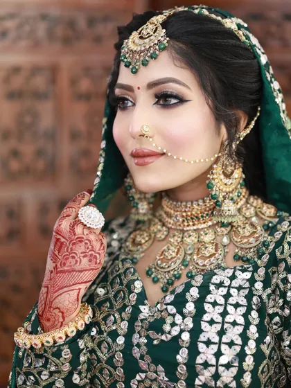 A gorgeous bride in a dark green lehenga. The makeup is classic glam, with a defined smokey eye and a nude lip.