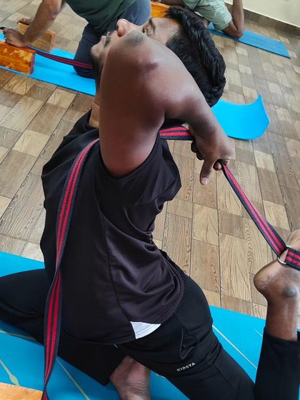 Another view of a student using a strap to achieve the full expression of Poorna Rajkapotasana, demonstrating advanced hip and shoulder flexibility.