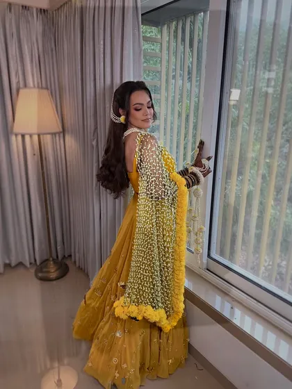 A radiant Haldi bride posing by the window. Her look is completed by my signature Tagar bud floral dupatta and matching jewellery.
