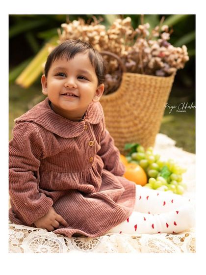 A happy, sun-kissed smile during an outdoor picnic-themed first birthday shoot. The natural light and greenery make these milestone portraits feel so warm and alive.