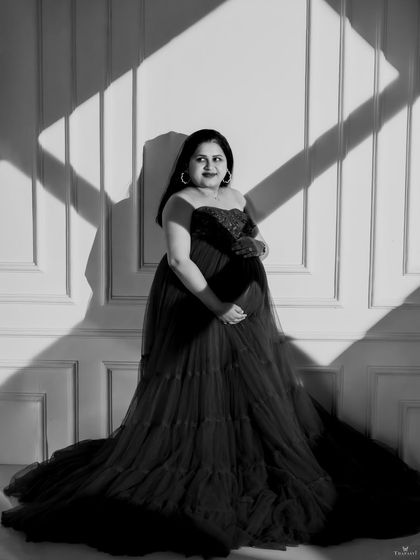 A striking black and white portrait using strong directional light. The play of light and shadow across the wall and the mom-to-be creates a bold, graphic, and artistic image.