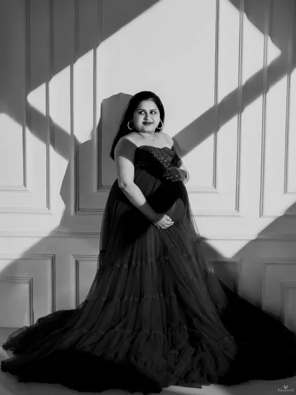 A striking black and white portrait using strong directional light. The play of light and shadow across the wall and the mom-to-be creates a bold, graphic, and artistic image.