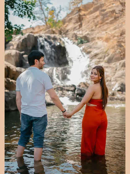 A "follow me to" style shot, with the couple wading into the cool water of a stream below a waterfall.