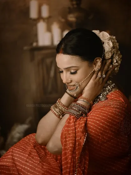 A dramatic bridal portrait using low-key lighting to create a moody and timeless feel. The focus is on the bride's quiet elegance, traditional jewelry, and the rich textures of her attire in a studio setting.