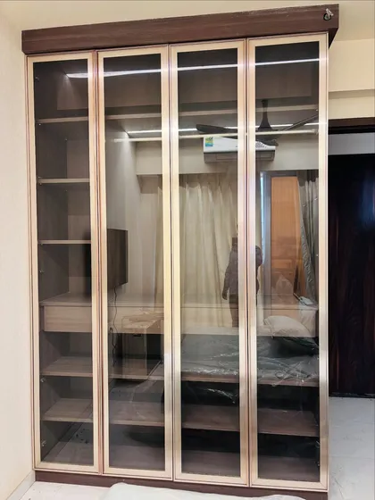 This elegant floor-to-ceiling wardrobe features tinted glass profile doors with a rich wood finish. The design offers a sophisticated way to display and organize your belongings, blending seamlessly into a modern bedroom aesthetic.