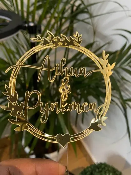 The "Aihun & Pynkmen" wreath topper held up, showing its intricate details and beautiful gold finish.