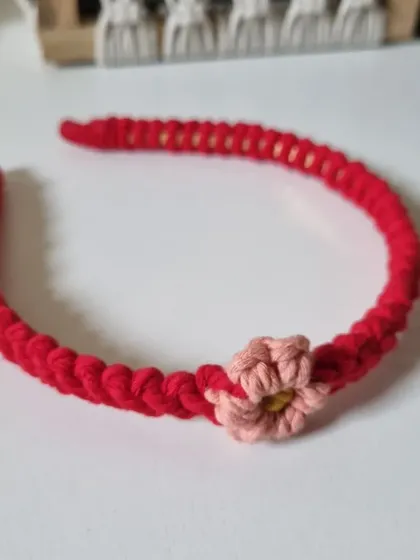 A single red macrame headband with a delicate pink flower. This piece is perfect for adding a pop of color and a touch of handmade charm to your hairstyle.