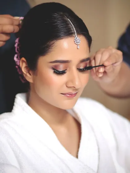 A behind-the-scenes moment of creating a regal bridal look. This shot captures the application of mascara, a final touch to make the eyes pop.