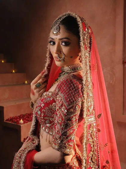The bride looks majestic with her red dupatta veiled over her head. The lighting creates a divine aura, highlighting her flawless makeup and intricate jewelry.