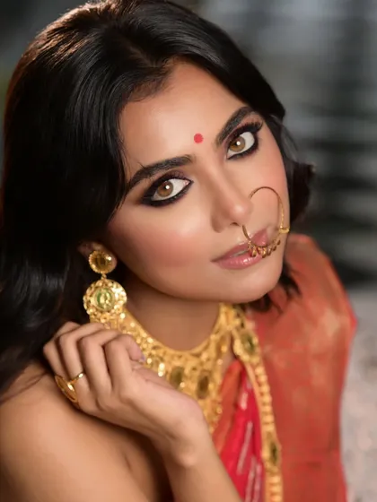A tight close-up focusing on the model's expressive eyes and traditional Bengali jewellery. This shot highlights the flawless makeup and the intricate design of the gold earrings and nose ring.