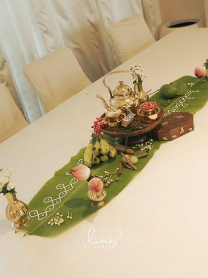 A high-angle view of the traditional table runner, with a brass tea set, bananas, and spices.