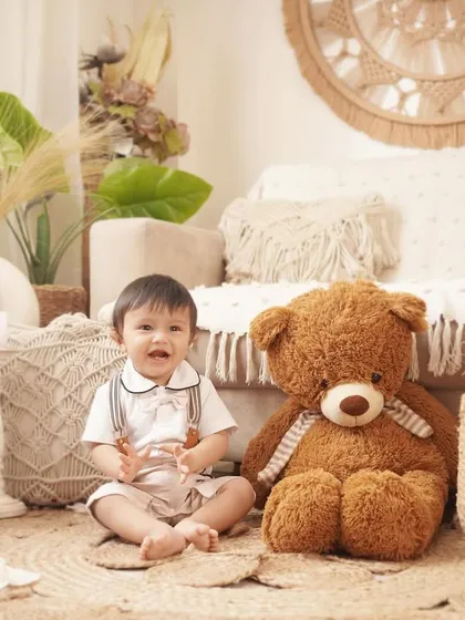 A baby boy sits with his giant teddy bear companion in a beautifully styled boho room for his first birthday photo session.