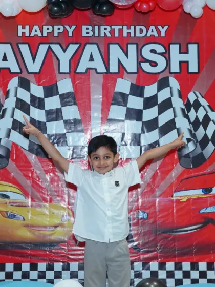 The birthday boy, Avyansh, strikes a powerful pose in front of his 'Cars' movie-themed backdrop. It's his day to be the star of the show.
