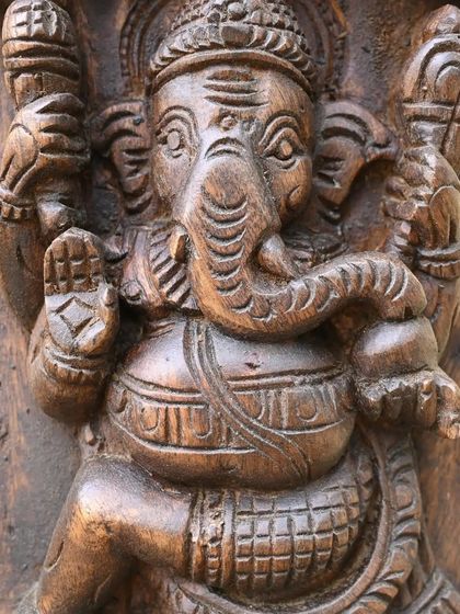 Another form of Ganesha from the vertical panel, this one in a seated posture of blessing. The dark wood grain adds texture and depth.