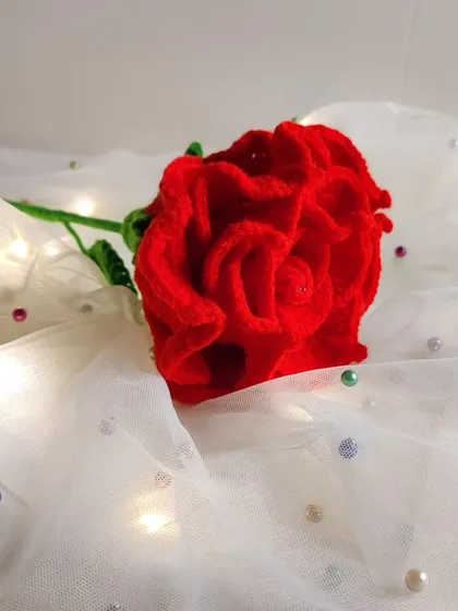 A slightly different angle of the crochet rose on the white fabric, with soft lighting.