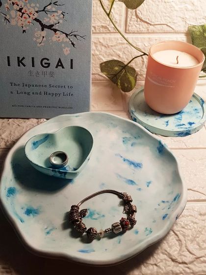 A set of concrete decor pieces in a blue marble finish, including a round plate tray, a mini heart dish, and a boundary coaster. Concrete gives a more rustic, earthy feel compared to Jesmonite.