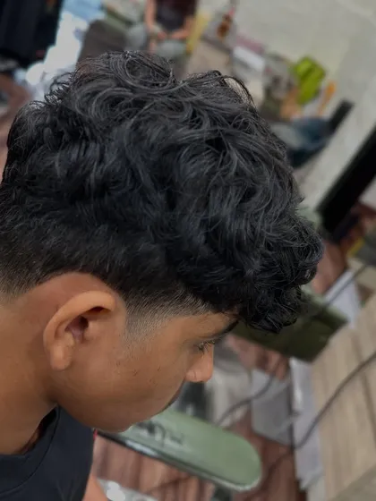 A side profile of a perfectly executed taper fade on curly hair. Learning to work with different hair textures is a key part of our advanced barbering curriculum.
