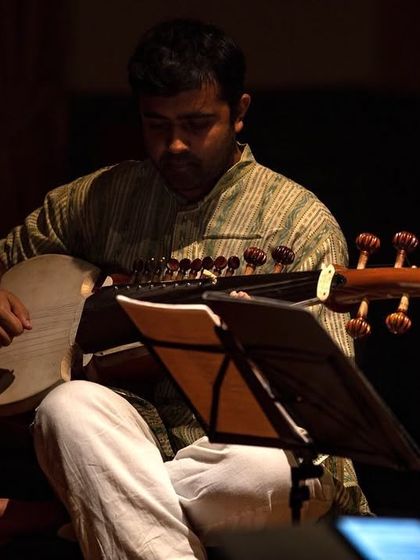 An artist playing the Sarod, an Indian classical instrument, during our 'Sangam' concert. The warm, focused lighting highlights the intricate details of the instrument and the musician's craft.