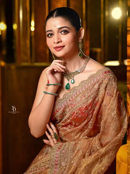 The same model now looks at the camera with a gentle smile. This shot is engaging and highlights the beauty of the emerald necklace and the intricate embroidery on the saree.