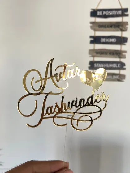 A beautiful cursive topper for "Avtar & Jashvinder," featuring their special date engraved in a small heart.