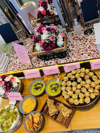 A wider view of our catering setup for Tira Beauty. The spread includes our deconstructed Papdi Chaat, Jalapeno Basil Hummus, and Khari with Cheese Broccoli Dip, all beautifully arranged with floral decorations.