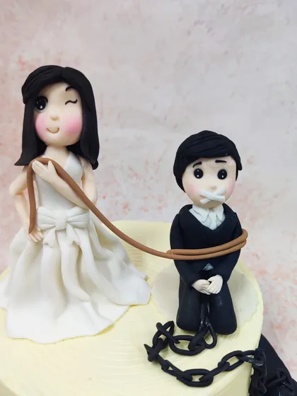 A close-up of the witty bride and groom toppers, showcasing the "ball and chain" detail with a heart lock.