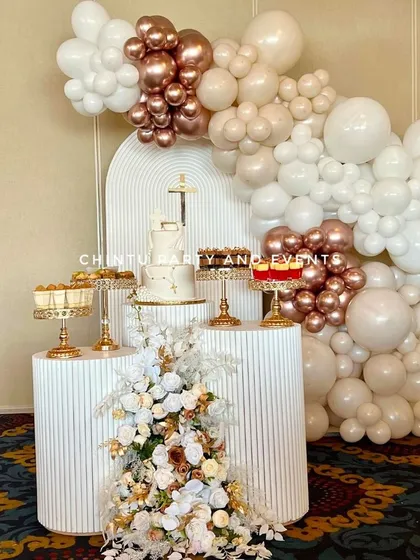A First Holy Communion decoration with a sophisticated color palette. The setup uses white, beige, and rose gold balloons with modern ridged pedestals.