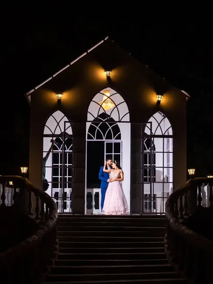 A wider view of the enchanting night scene. The lighting on the building creates a magical, almost theatrical, backdrop for this romantic couple portrait.