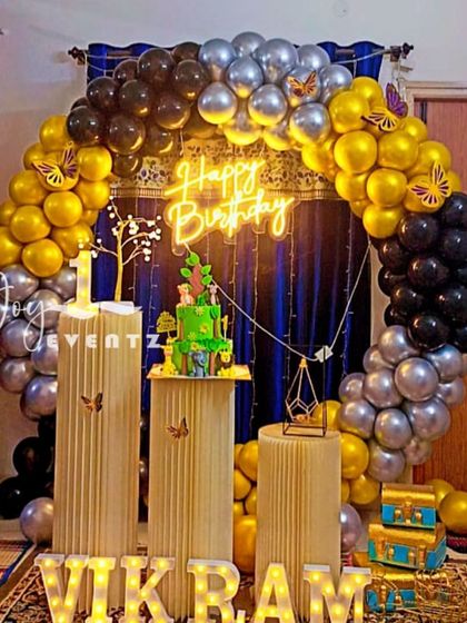 I created this elegant balloon ring decoration for Vikram's first birthday. The arch of gold, black, and silver balloons is set against a dark curtain, with fluted plinths for the cake and light-up marquee letters.