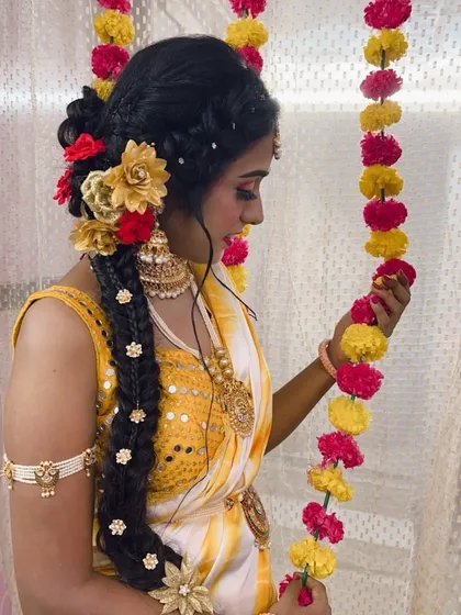 A side profile of the Haldi ceremony look, showing the intricate braid decorated with both real and artificial flowers. This angle highlights the detailed hair work and how it complements the overall traditional attire.