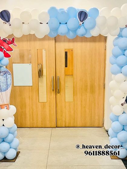An impressive entrance arch for an airplane-themed party. The doorway is framed with blue and white balloons resembling clouds, with airplane and hot air balloon cutouts.