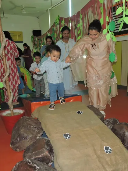 A mother guides her toddler across a jungle-themed obstacle course. Our family events include age-appropriate physical activities that are both safe and exciting for our youngest learners.