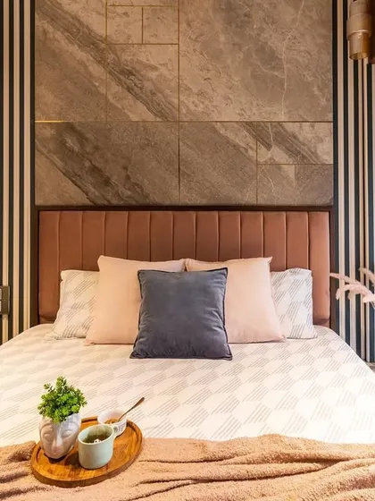 A bedroom that strikes a perfect balance between bold patterns and soft textures, with a striped and stone-tiled feature wall behind a plush pink headboard.