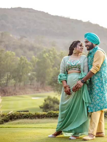 A full view of the couple in their stunning traditional attire, standing in a picturesque green landscape. This photo captures the elegance and grandeur of a destination pre-wedding shoot.