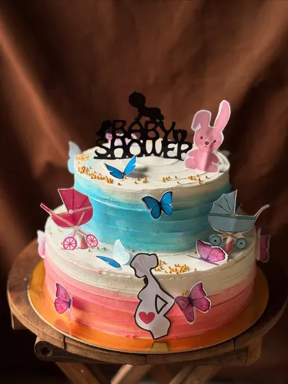 A lovely two-tier cake for a baby shower. The pink and blue watercolor effect is perfect for a gender reveal, decorated with cute baby-themed toppers.