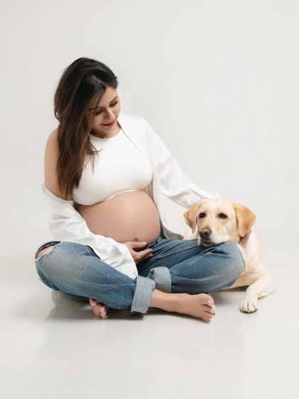 A serene portrait of the expecting mother sitting with her dog, her hand resting gently on her belly. This captures the quiet anticipation and the bond with her first baby.