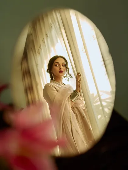 A creative shot for AR by Rhea Kapoor, using a mirror to frame the model's reflection. The composition is layered and romantic, with soft light filtering through a window.